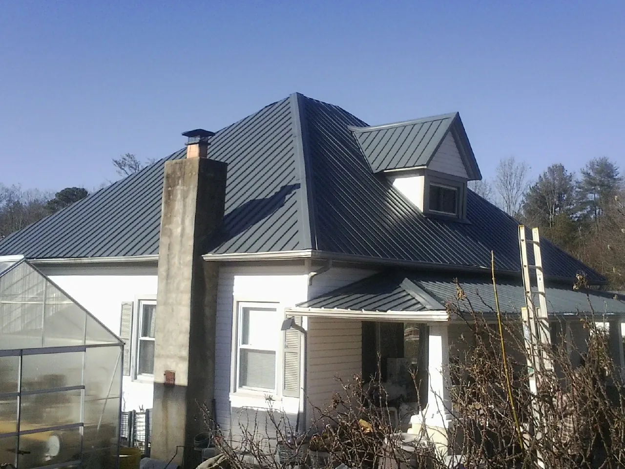 Dark blue standing seam metal roof on a white farmhouse with dormer — Slate & Tile Roof Repair by Roofing Brothers in New Hartford