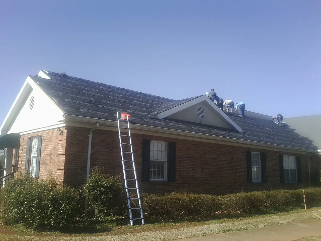 Crew tearing shingles off a brick ranch roof with a ladder set — Metal Roof Repair work by our crew in New Hartford