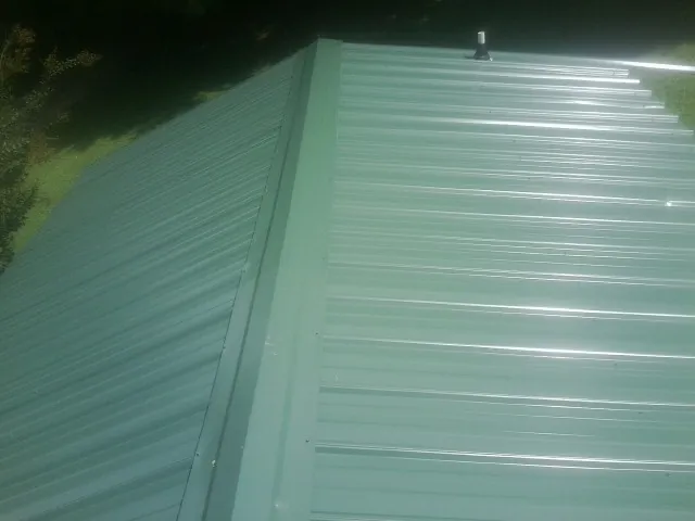 New green metal panels meeting at the ridge of a roof — Flat Roof Repair work by our crew in New Hartford