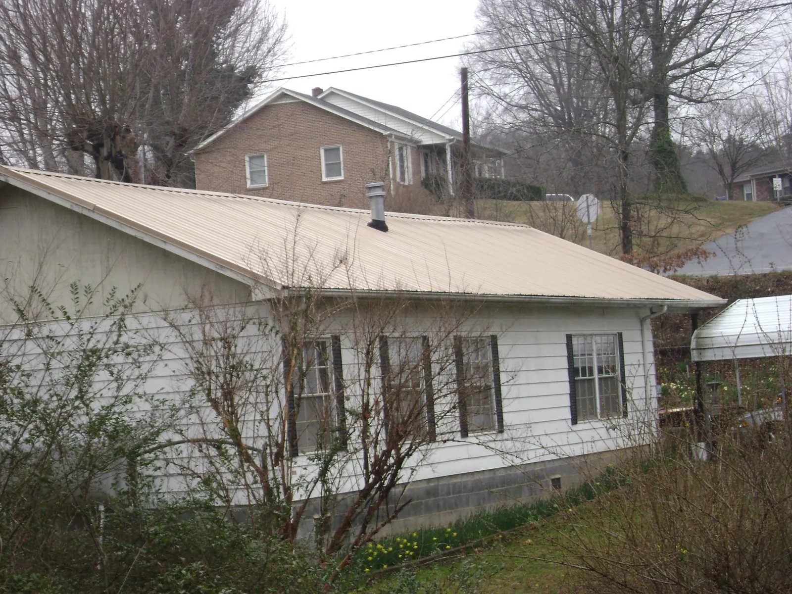 Tan metal roof on a white sided house set into a hillside — Commercial Roofing by Roofing Brothers in New Hartford
